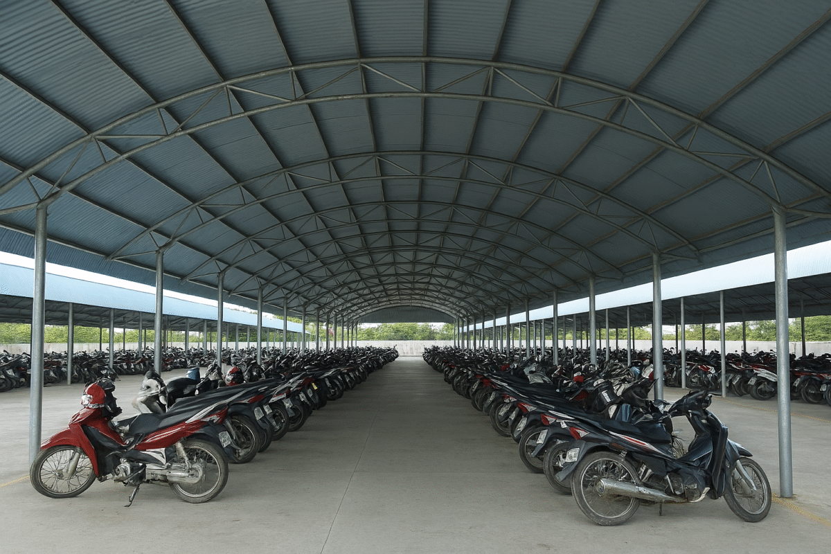 Nhà xe mái vòm tôn lạnh khung thép hộp tại nhà xưởng, nền bê tông sạch, xe máy đậu gọn gang.